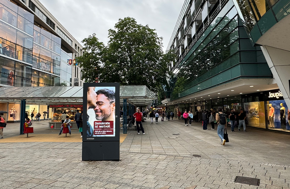 Eine belebte Einkaufsstraße mit Menschen, Geschäften und einem großen Werbeplakat.
