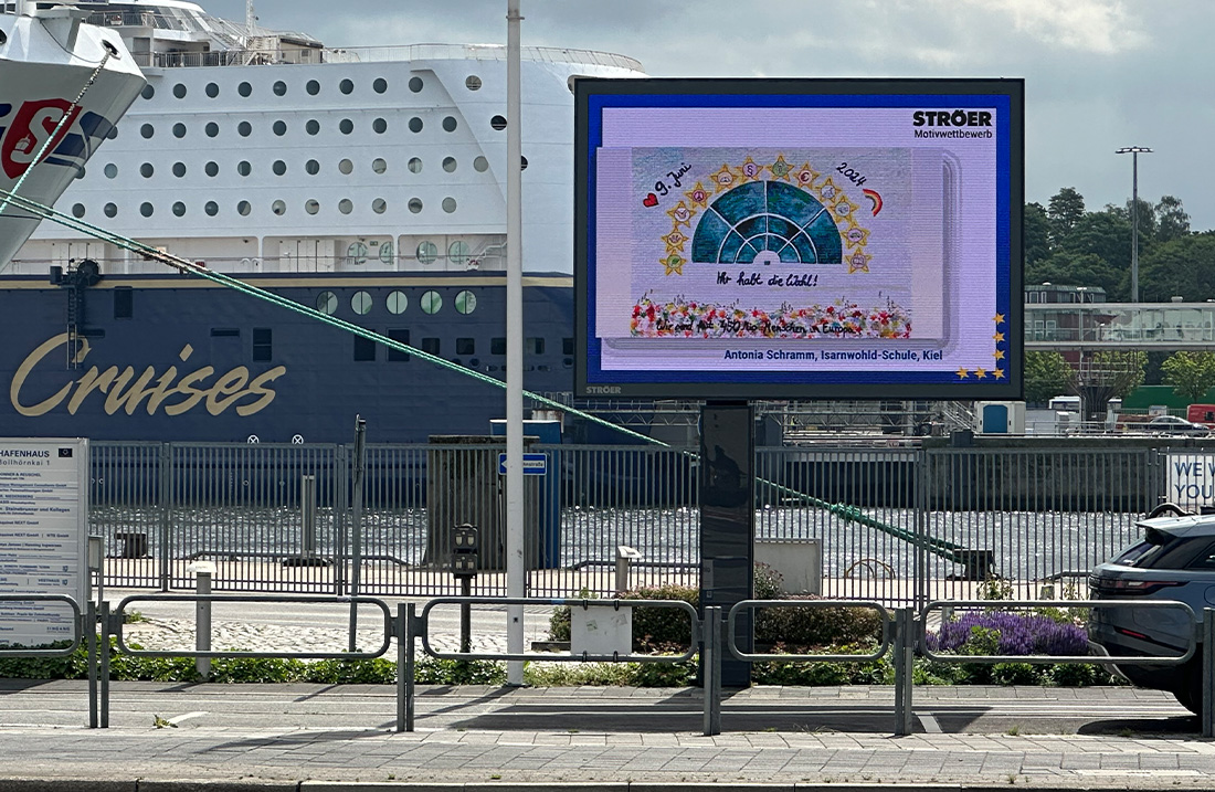 Eine digitale Werbetafel mit einem bunten Kinderbild, im Hintergrund ein großes Kreuzfahrtschiff.