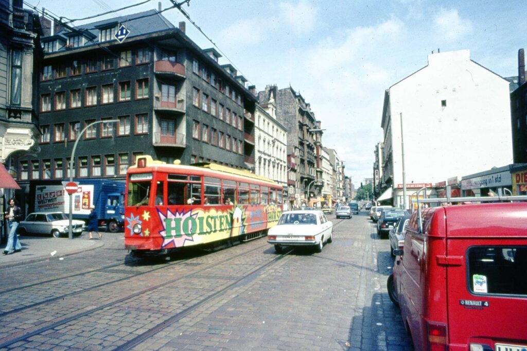 Eine bunte Straßenbahn in einer geschäftigen Stadtstraße mit älteren Gebäuden im Hintergrund.