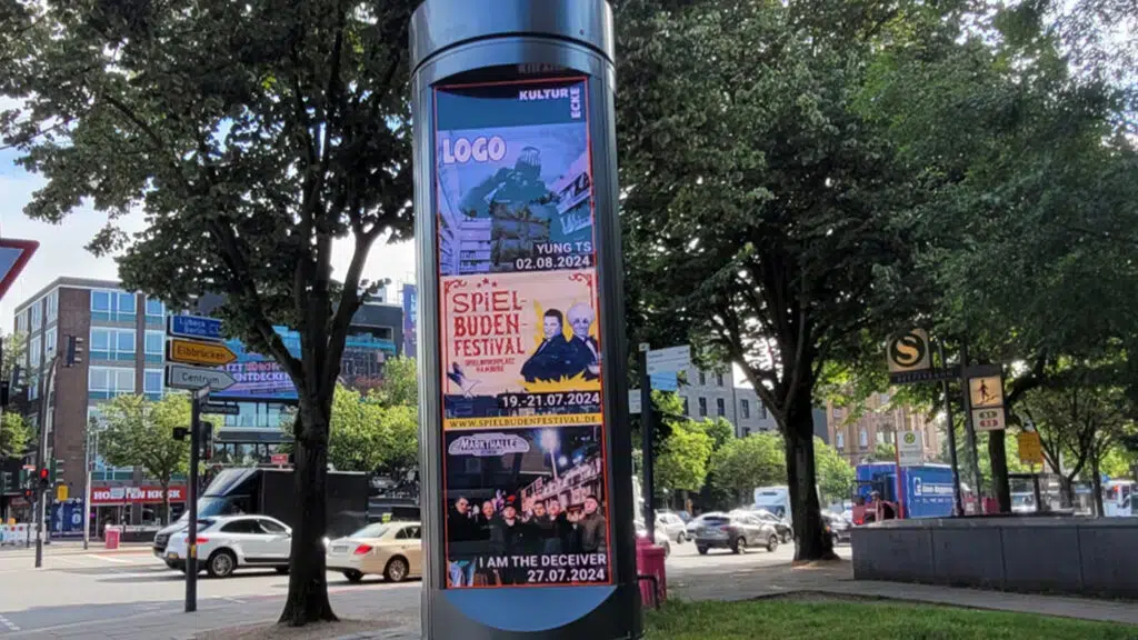 Drei bunte Veranstaltungsplakate mit fröhlichen Menschen an einer Litfaßsäule im Freien